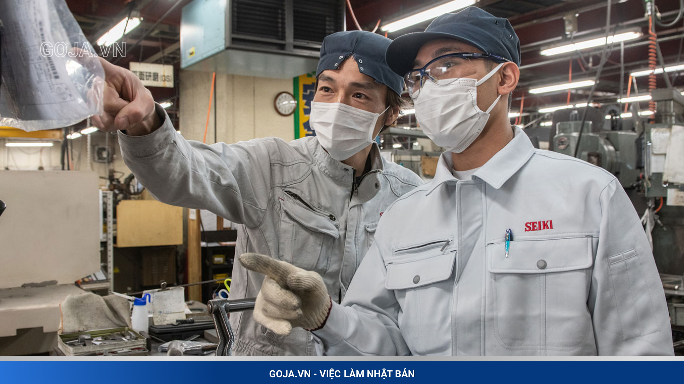 Thủ Tục Đi XKLĐ Nhật Bản 2026 Theo Bộ Lao Động: Hướng Dẫn A–Z Hai kỹ thuật viên trao đổi tại xưởng sản xuất cho thấy môi trường làm việc chuyên nghiệp và an toàn dành cho lao động Việt Nam lựa chọn đi XKLĐ theo Bộ Lao Động năm 2026.